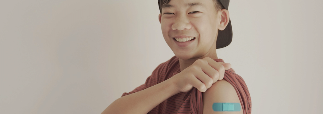  young male asian teenager with a backwards hat smiling after reciving a shot with a bandaid on his arm